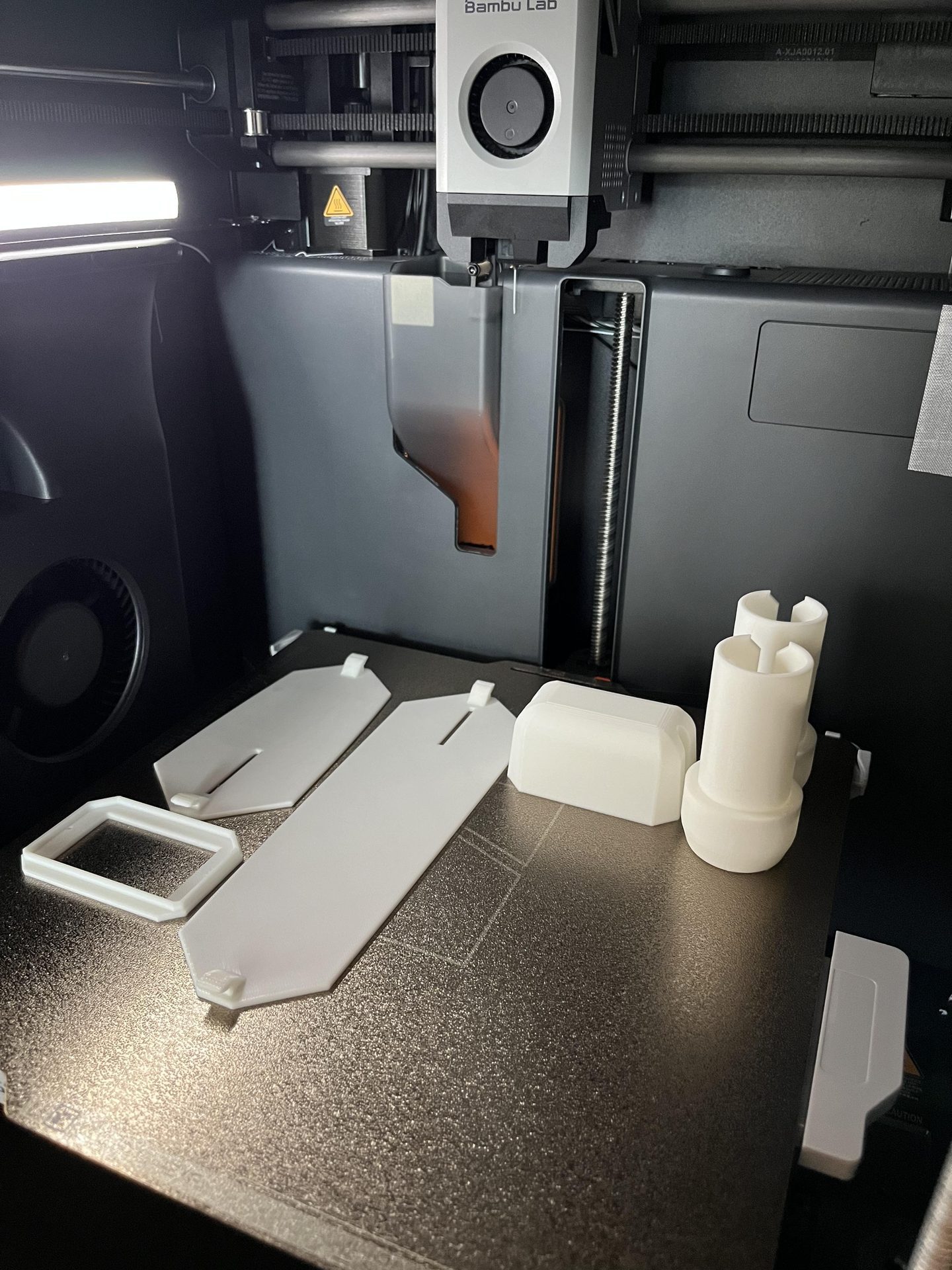 Bambu Lab printer with white drone parts on bed